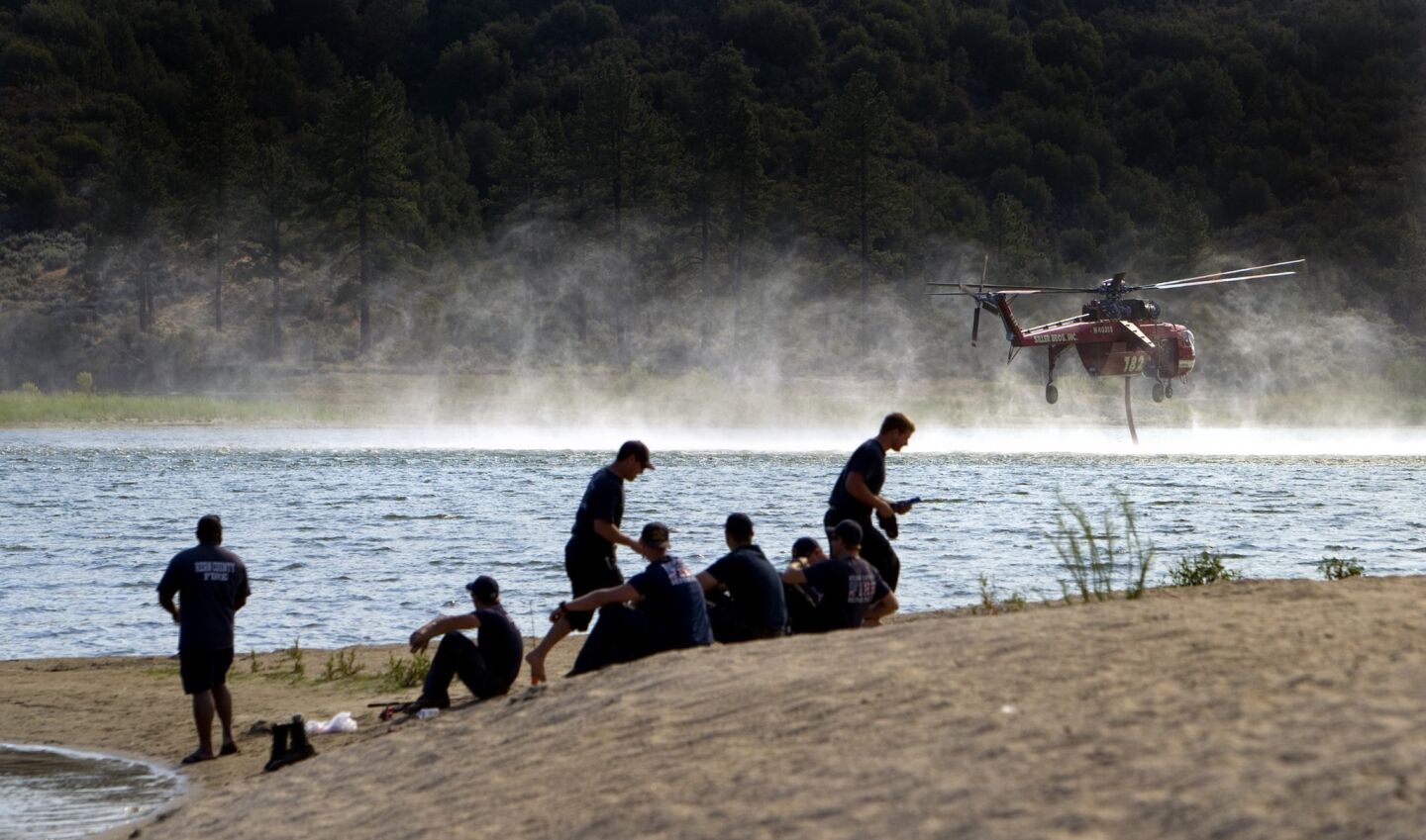 Kern County firefighters take a break on the shores of Lake Hemet as a water-dropping helicopter refills during the Mountain fire off Highway 74.