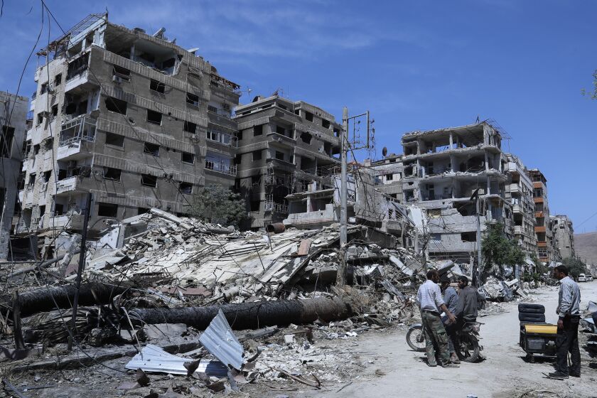 FILE - People stand in front of damaged buildings, in the town of Douma, the site of a suspected chemical weapon attack, near Damascus, Syria, on April 16, 2018. Syria on Thursday Feb. 2, 2023 dismissed the findings of an investigation of which the global chemical weapons watchdog concluded that there were “reasonable grounds to believe” Syria’s air force dropped two cylinders containing chlorine gas on the city of Douma in 2018. (AP Photo/Hassan Ammar, File)