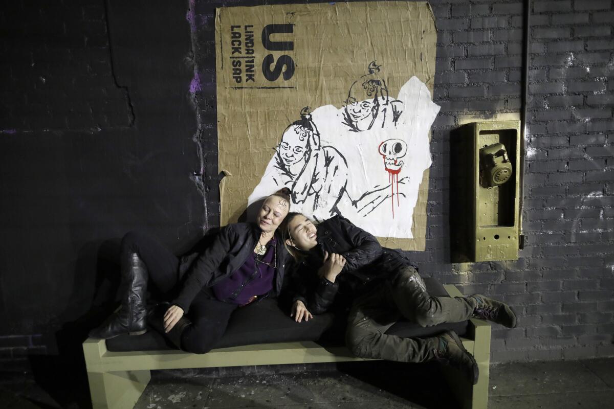 Dance instructor Linda Lack and street artist Inksap huddle on a bench under one of their posters on Anderson Street in downtown Los Angeles.