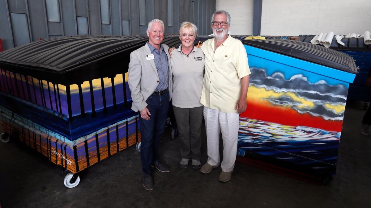 City Councilman Patrick Brenden, left, and Huntington Beach Public Art Alliance co-founders Barbara Haynes and Kim Kramer pose with some of the trash bins in the Dumpsters on Parade project.