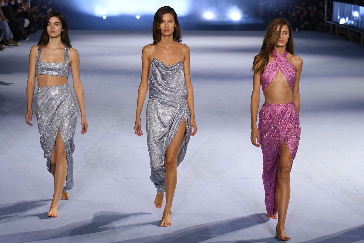Three models in draped metallic clothing on a runway