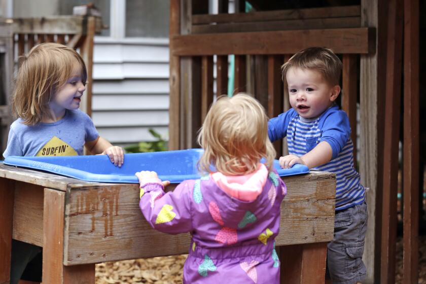 In this photo taken Monday, Aug. 27, 2018, Astrid Kozlen, left, and Vincent Seeborn, right, talk with another toddler at a splash bin in the playground at the Wallingford Child Care Center in Seattle. A dire workforce crisis in a booming U.S. economy is forcing many in the child care industry to turn to business tactics more closely resembling Wall Street than Sesame Street. Non-compete and "hold-harmless" legal agreements, college tuition incentives for workers and steep waiting-list fees for parents are fast becoming the norm. (AP Photo/Elaine Thompson)