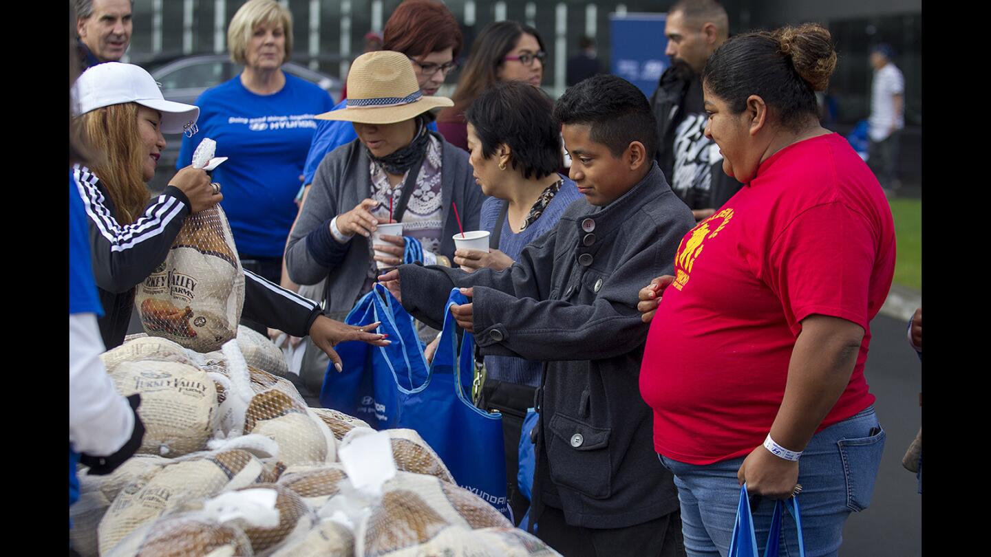 Jorge Bailon, with his mother, Marian, right, receives a free turkey from Loraine Cook during a free turkey giveaway at Hyundai Motor America headquarters in Fountain Valley on Saturday.