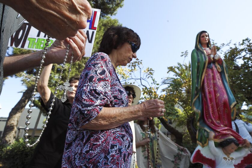 People protesting against the Drag Queen Story Hour hold rosary beads while praying next to a statue of Our Lady of Guadalupe at the Chula Vista Public Library Civic Center Branch on Tuesday, September 10, 2019 in Chula Vista, California.
