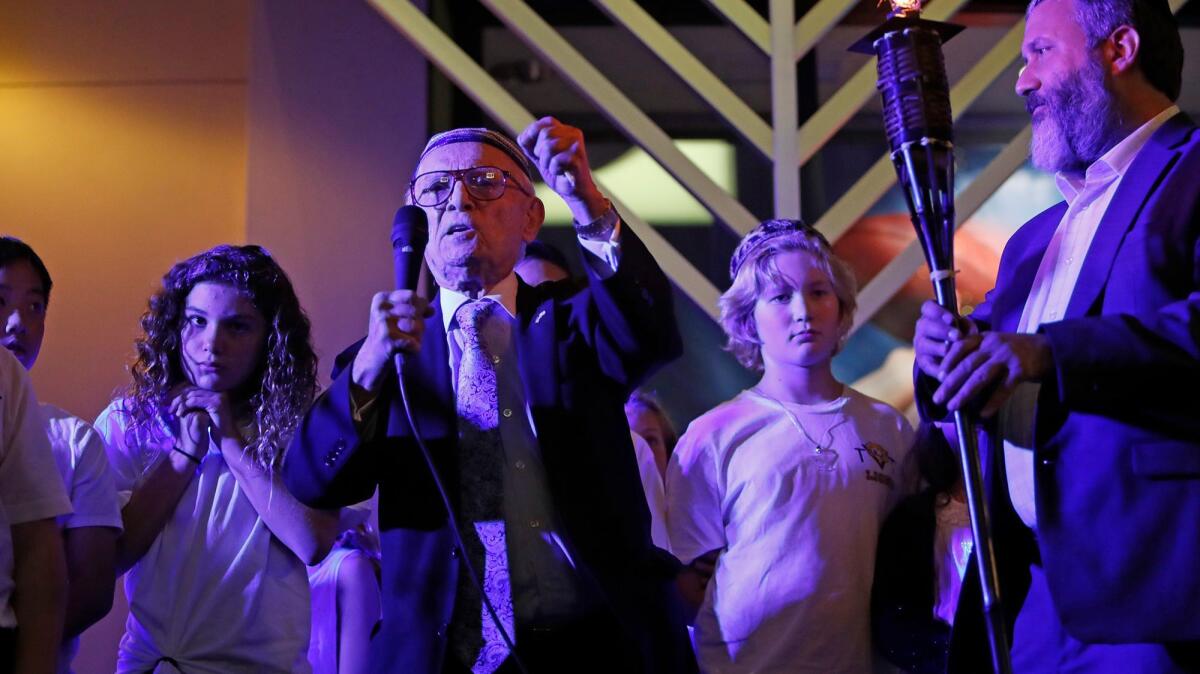 Keynote speaker Dr. Jacob Eisenbach, left, a 93-year-old Holocaust survivor, talks during the menorah lighting ceremony celebrating the first night of Hanukkah at Fashion Island on Tuesday in Newport Beach. At right is Rabbi Reuven Mintz with the Chabad Center for Jewish Life.