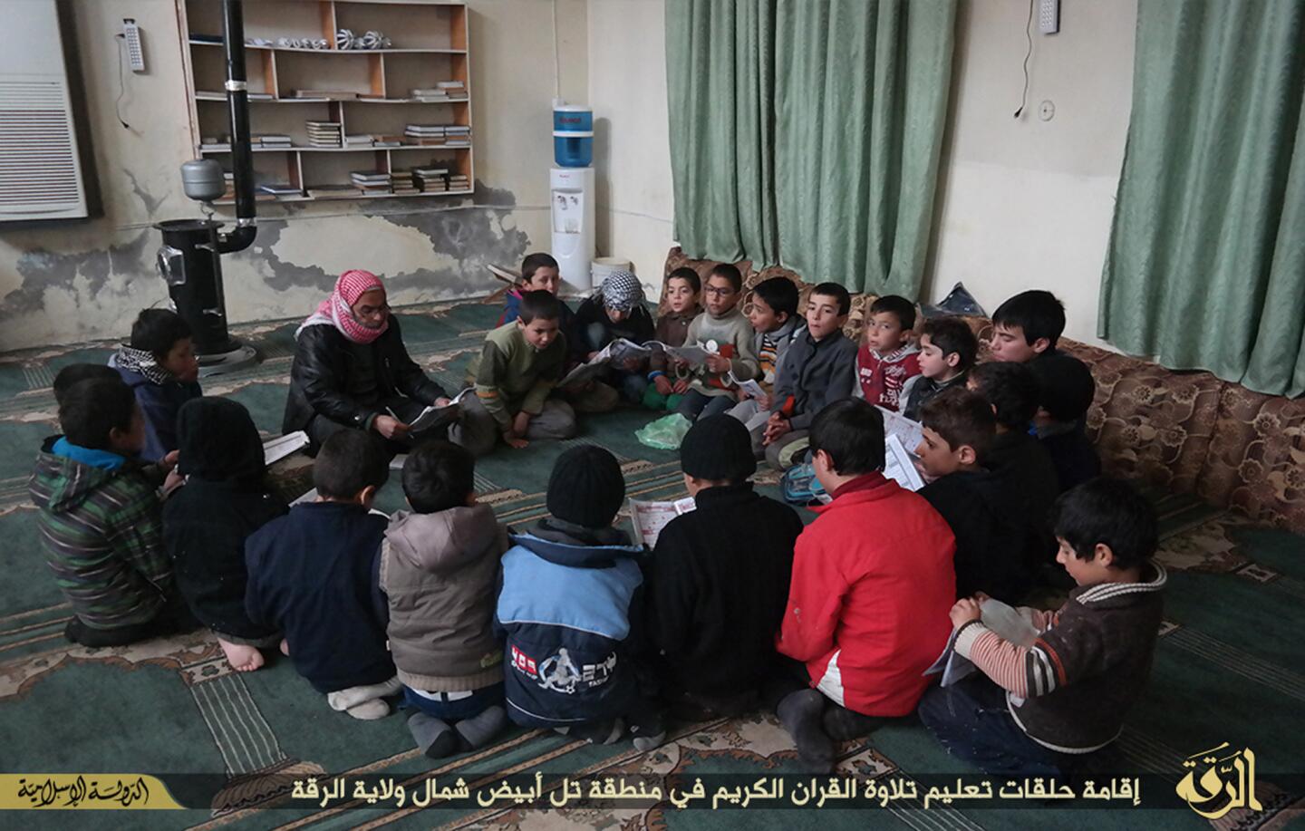 In this photo released on Jan. 13, 2015, by a militant website, which has been verified and is consistent with other AP reporting, an Islamic State preacher, center left background, gives lessons to Syrian boys in how to recite the Quran, in Tel Abyad, in Raqqa province, northeast Syria.