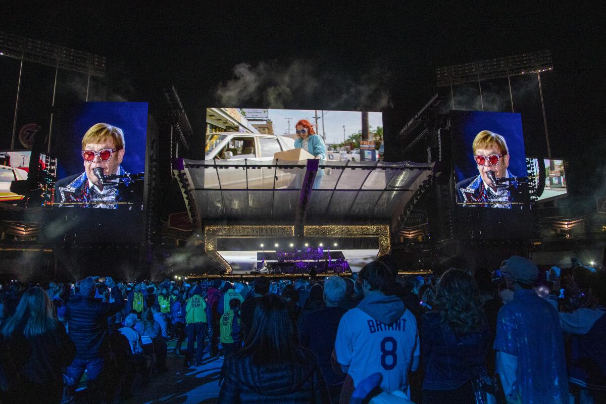 People stand in a darkened stadium as Elton John sings.
