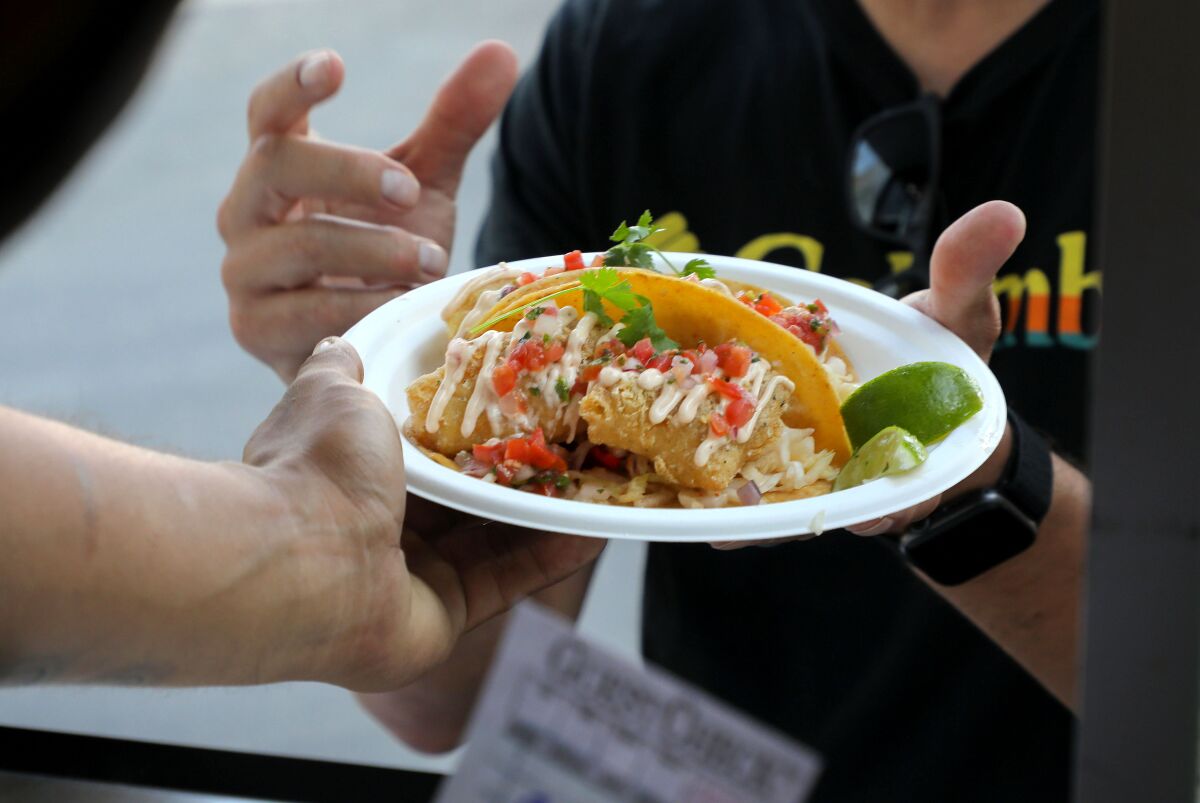Una clienta recibe su plato de tacos veganos de pescado en el remolque de comida SeaCo Catch.