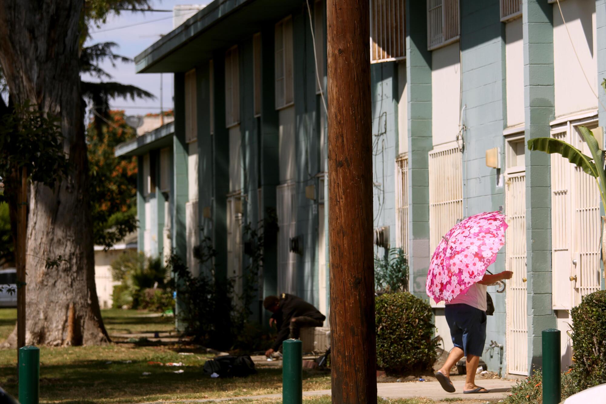 A woman with a pink umbrella walks to an apartment building.