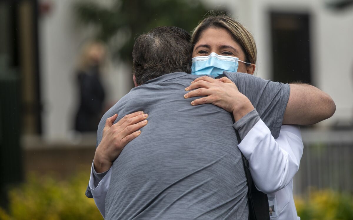 A man hugs a doctor wearing a mask and white coat.