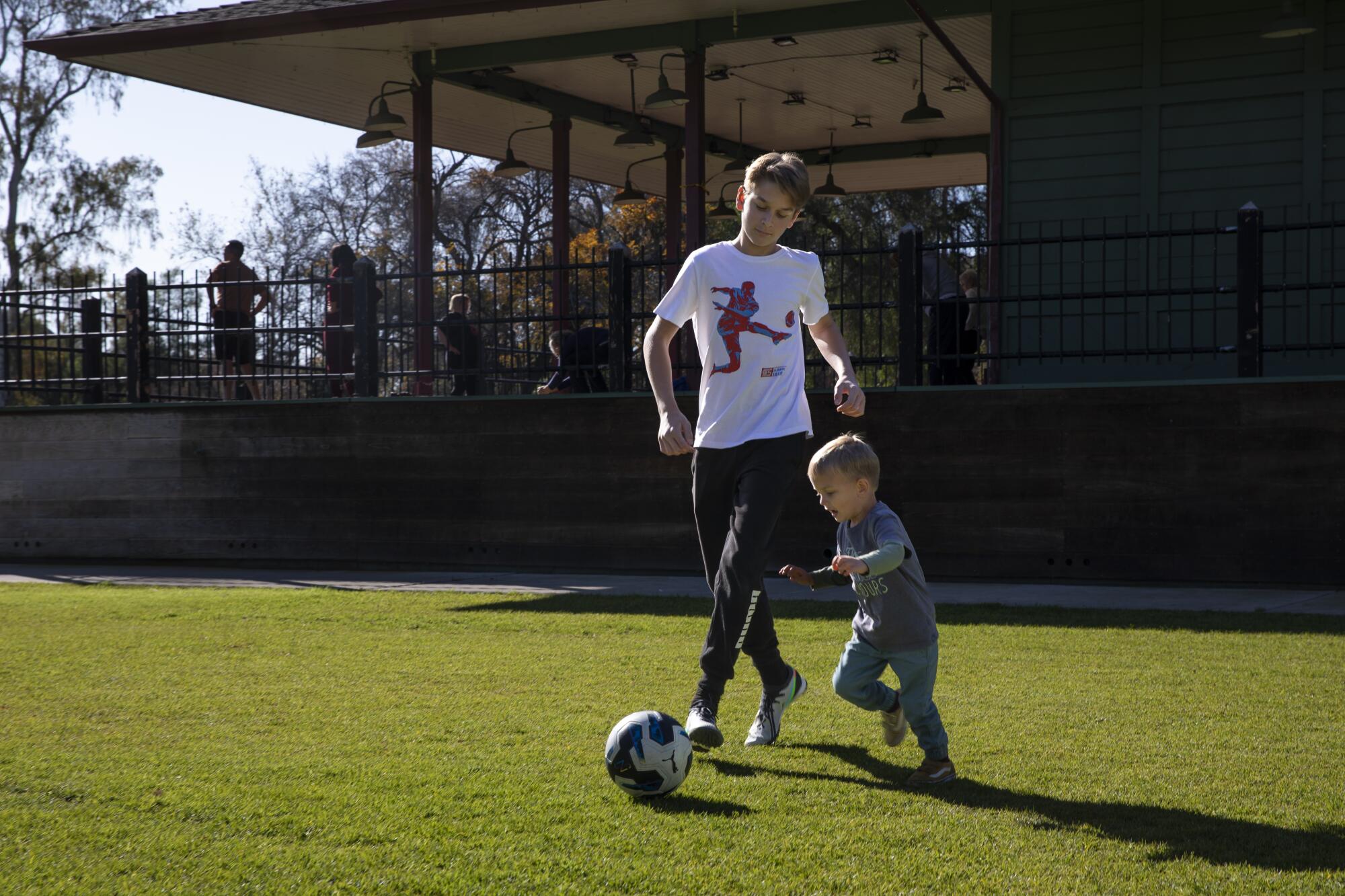 Two boys — a teenager and a toddler — play with a soccer ball