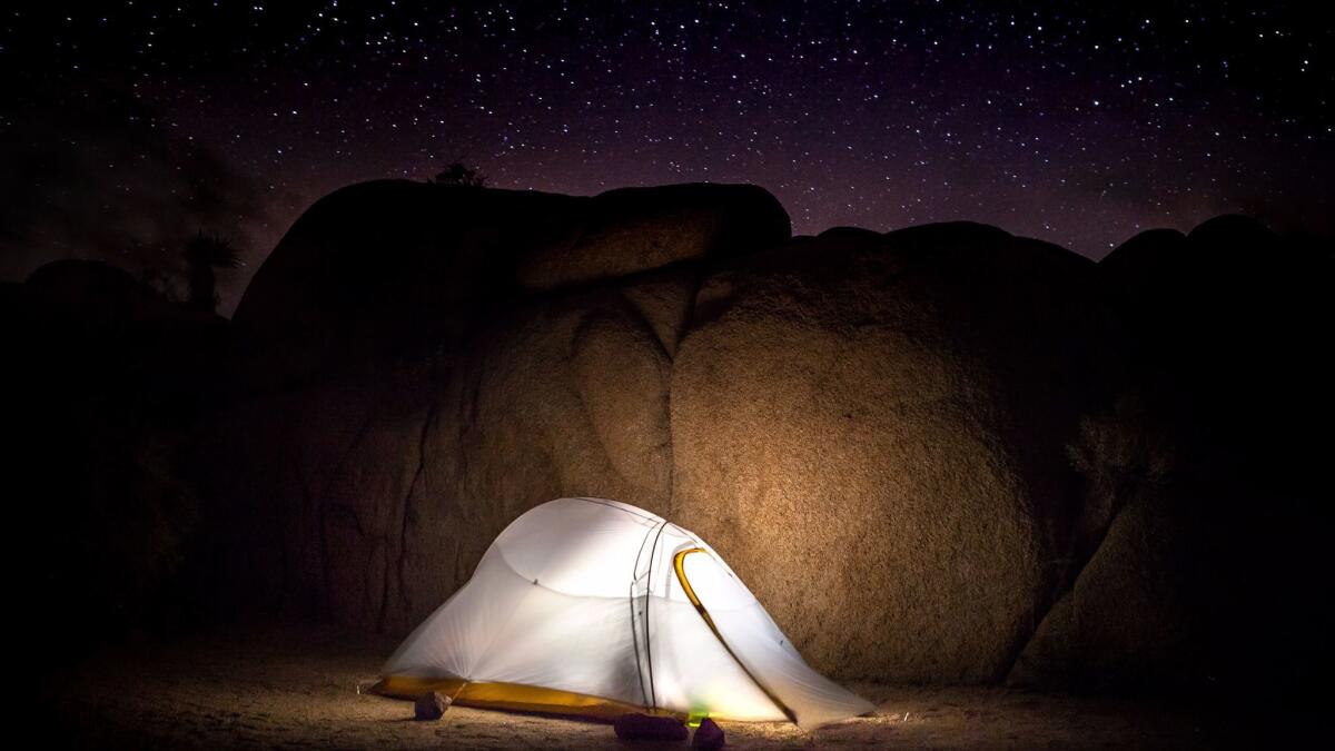 The glow of a tent camp light casts on the large boulders shielding the heavy winds on a starry night at the Jumbo Rocks Campground in Joshua Tree National Park. (GaryKavanagh / Getty Images/iStockphoto)