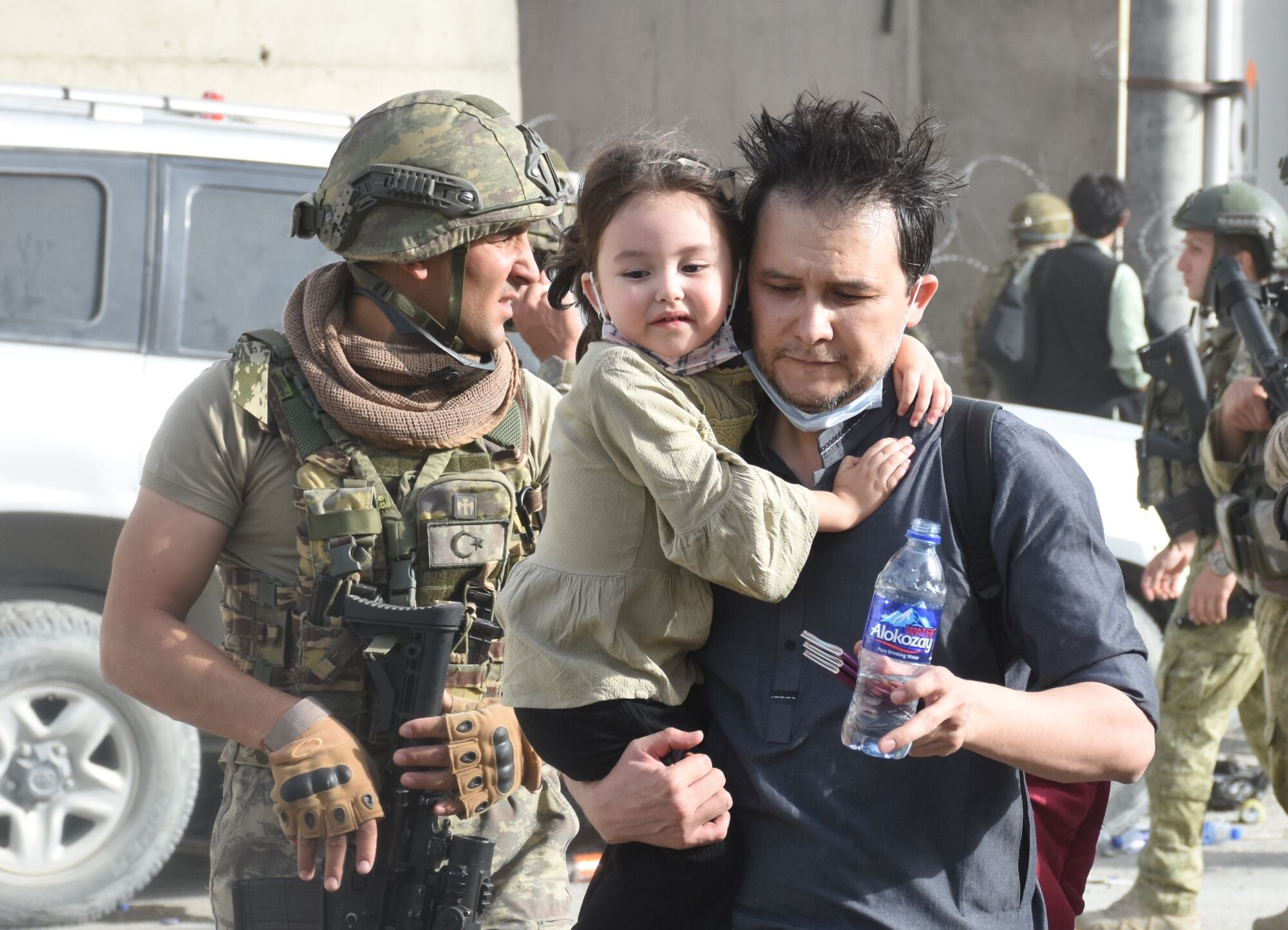 Accompanied by soldiers, a man carries a small child