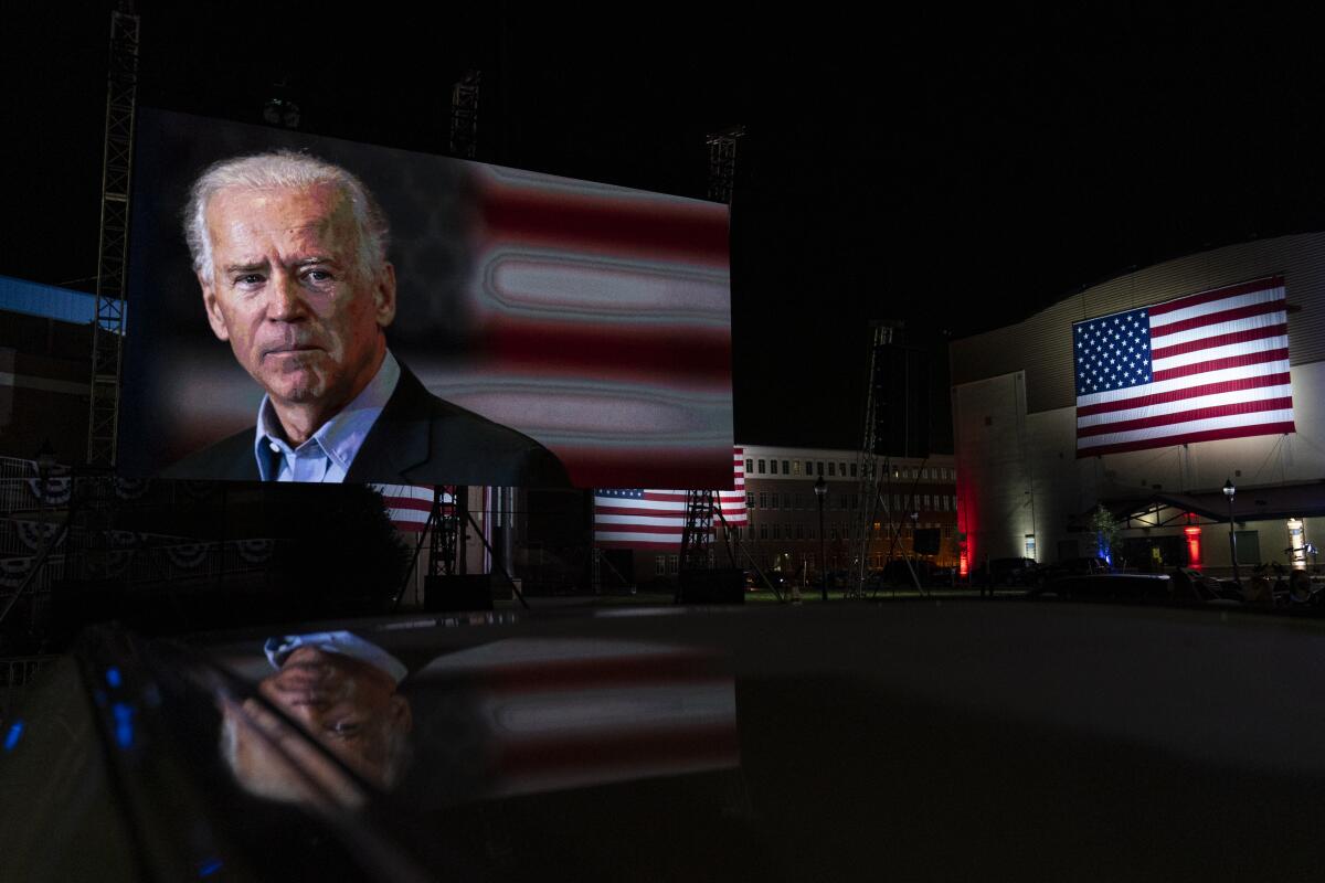 Joe Biden appears on a giant screen outdoors.