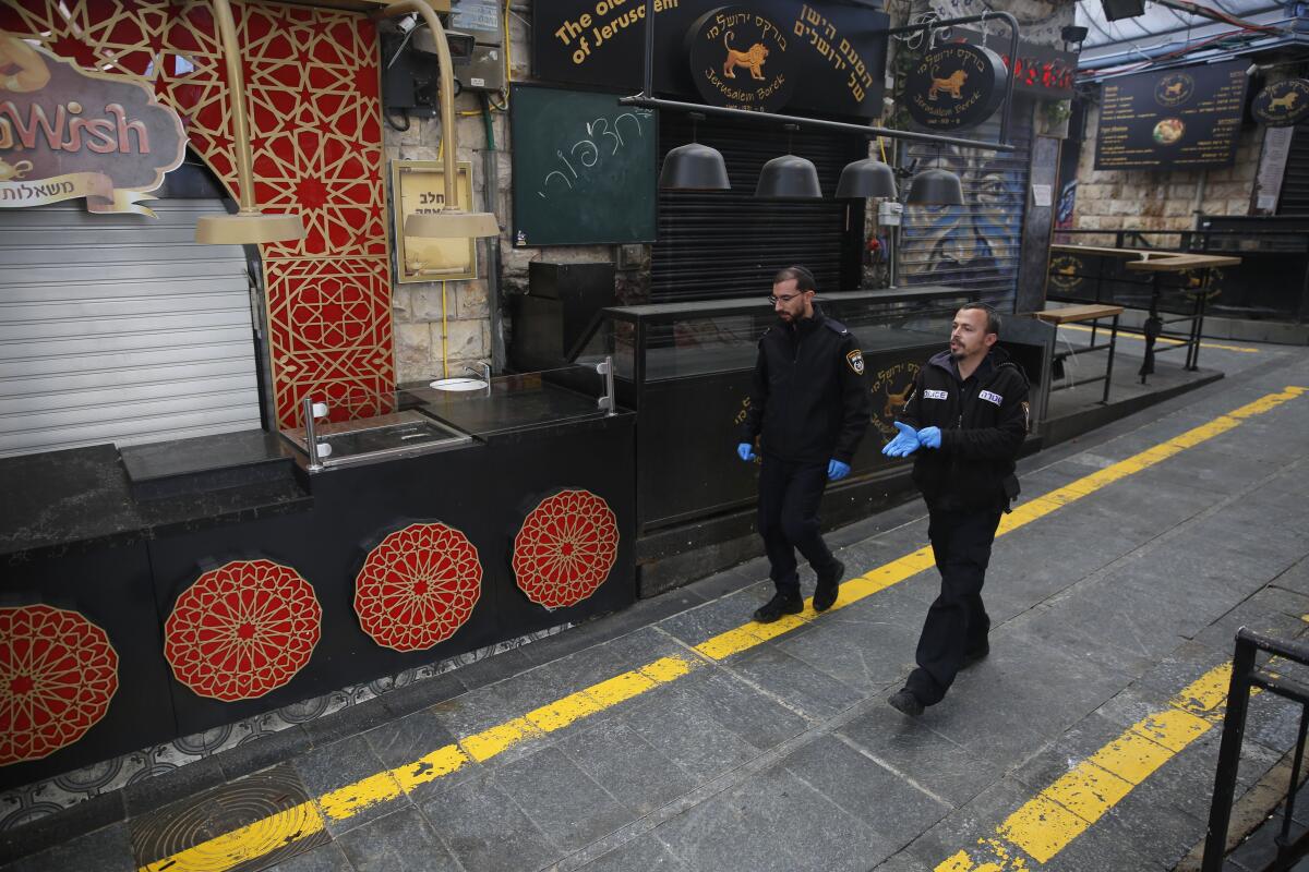 Israeli police officers walk past shuttered stores after authorities asked shop owners to close, in an effort to reduce the spread of the coronavirus, at a market in Jerusalem on Sunday.