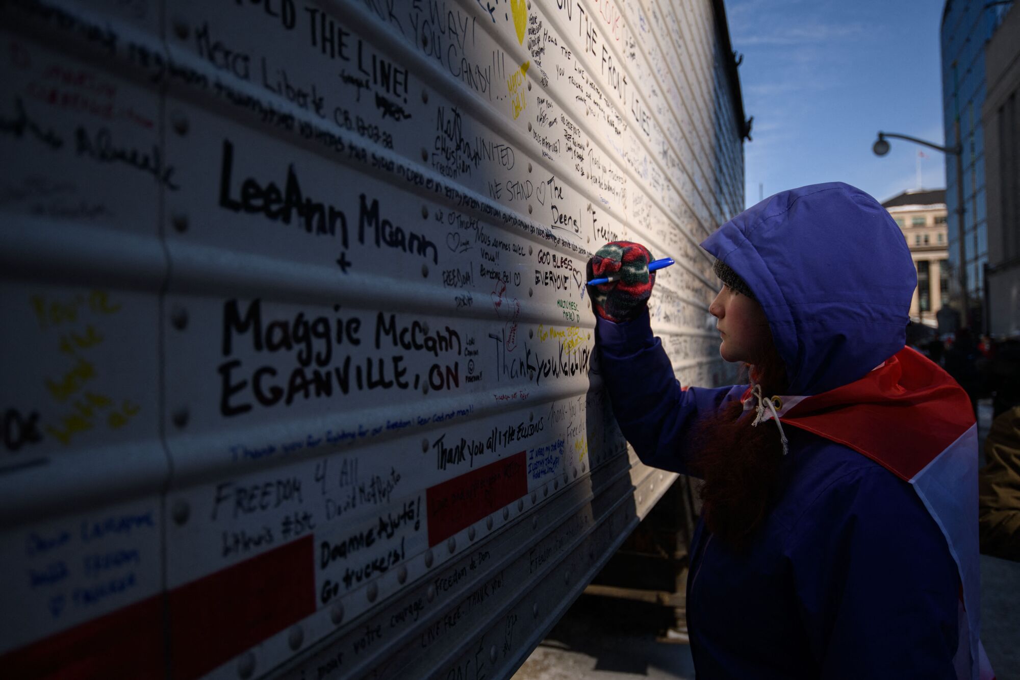 A person writes a message, alongside many other messages, on the side of a truck 