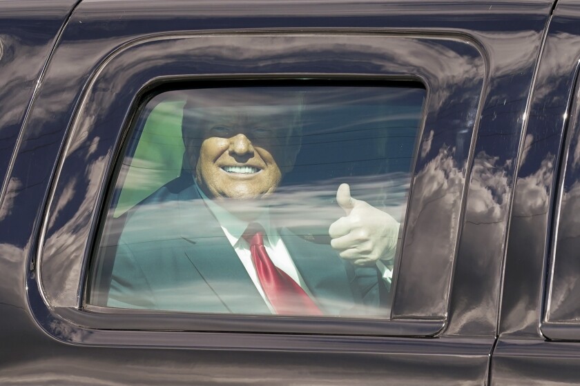 Trump, inside vehicle, smiles and gives a thumbs up.