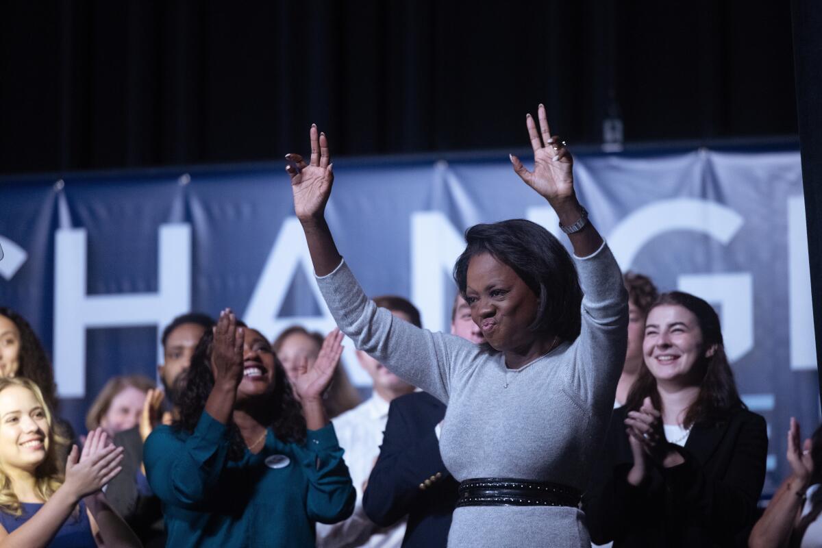A woman with pursed lips raises both hands above her head at a rally.
