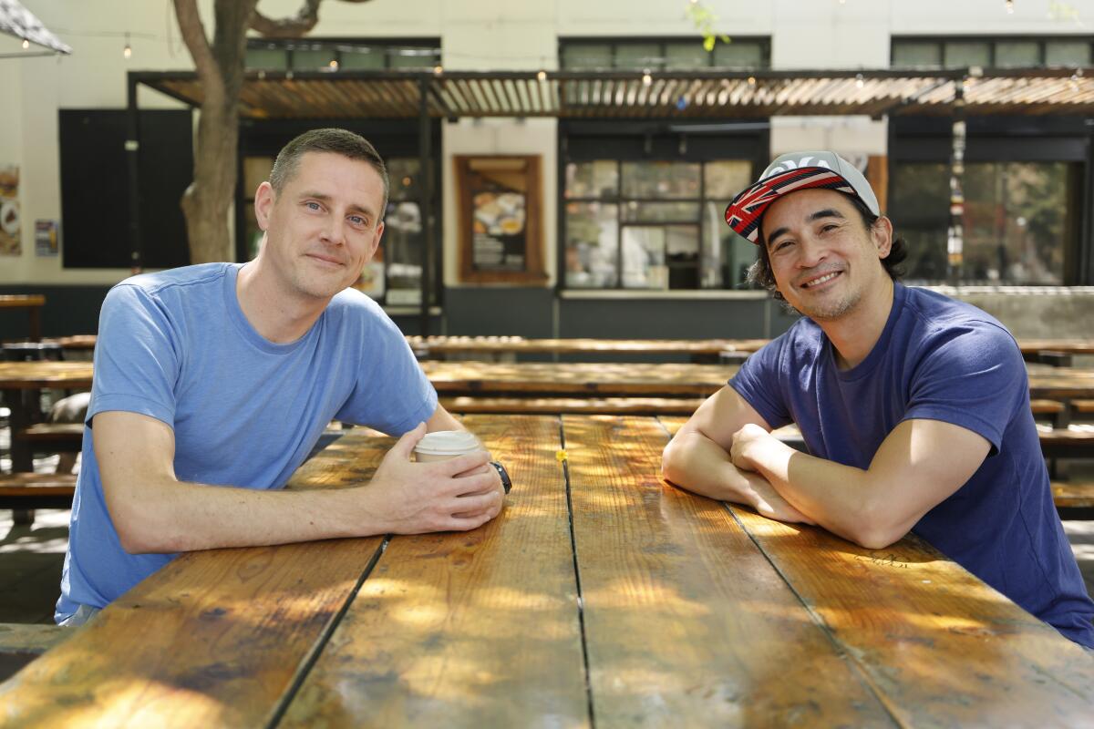 Two men sit at a wood table on a patio.