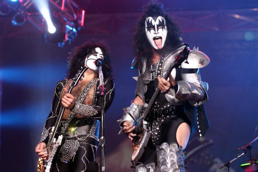 Two men with long, black hair wearing studded outfits and black-and-white face paint while playing guitar