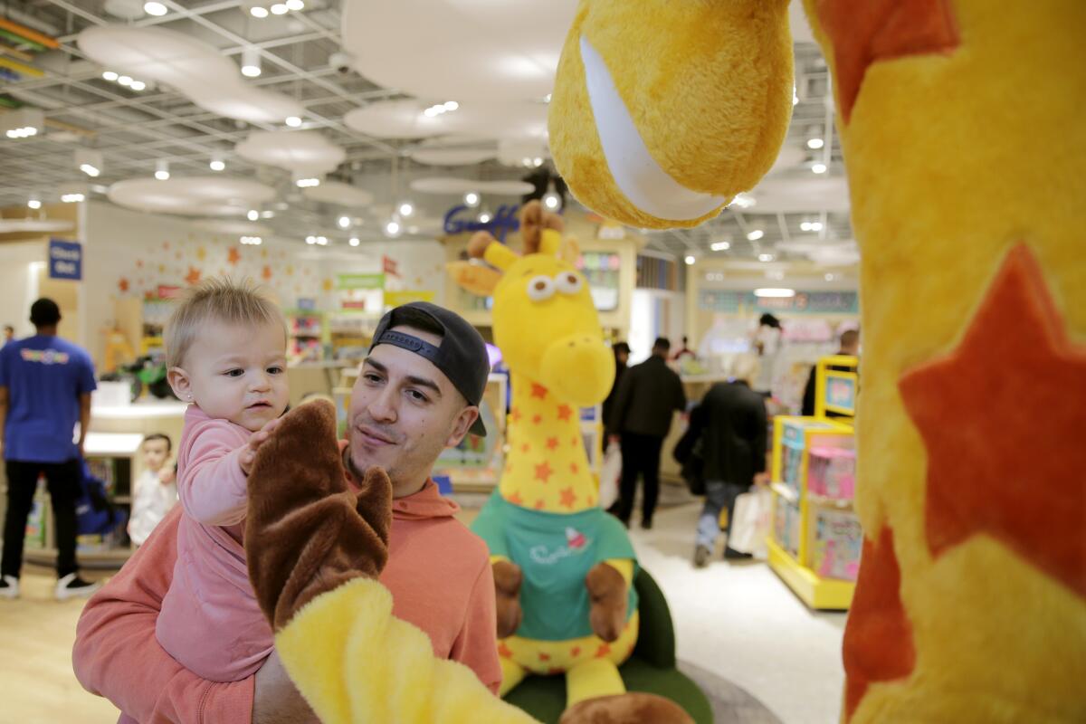 A father and baby greet Toys R Us mascot Geoffrey
