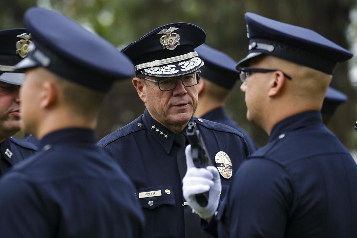 Several police officers standing for inspection as an official stops in front of one holding a gun in his white-gloved hand