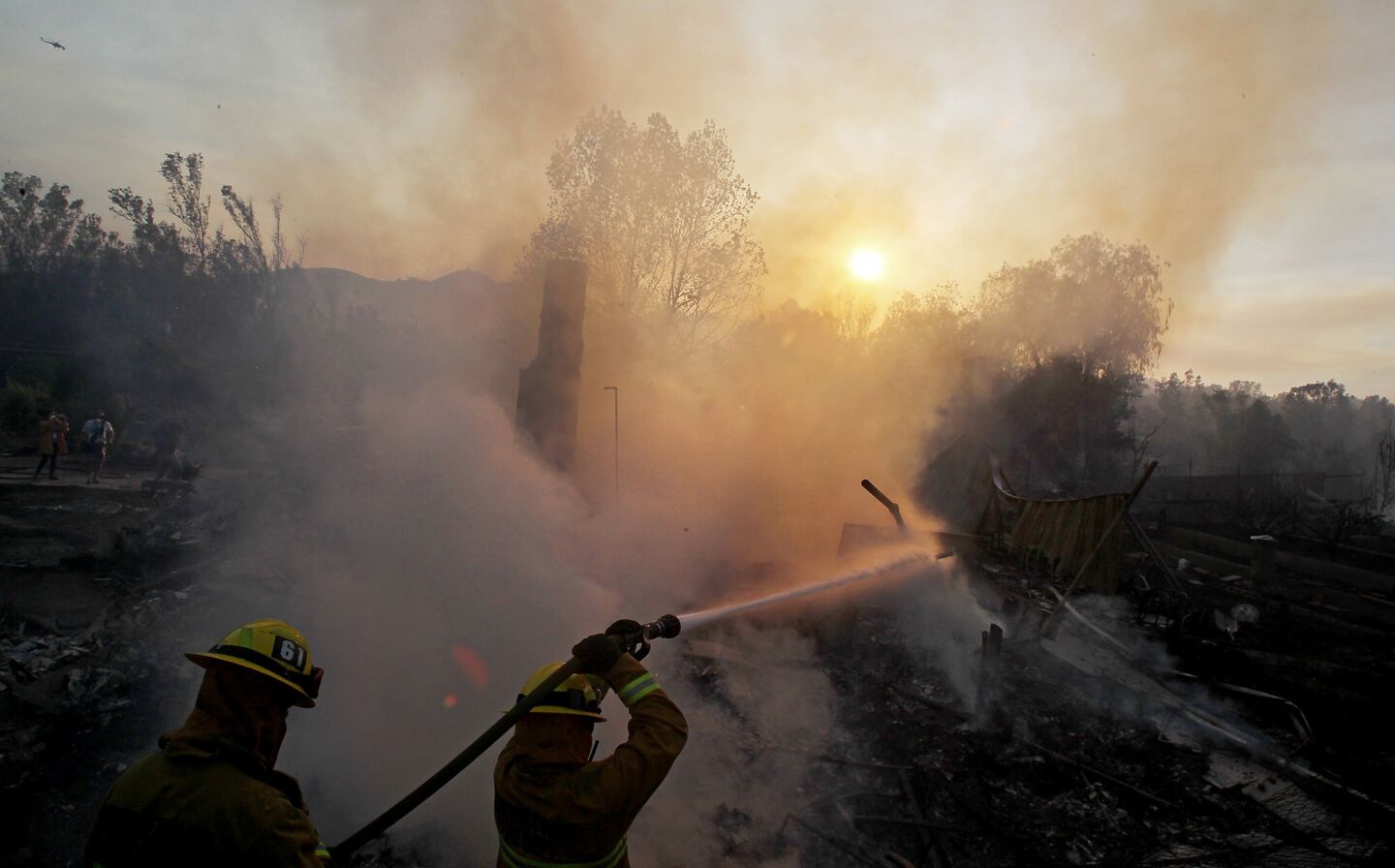 Firefighters hose off the smoldering ruins of a home along Country Club Drive in Escondido.