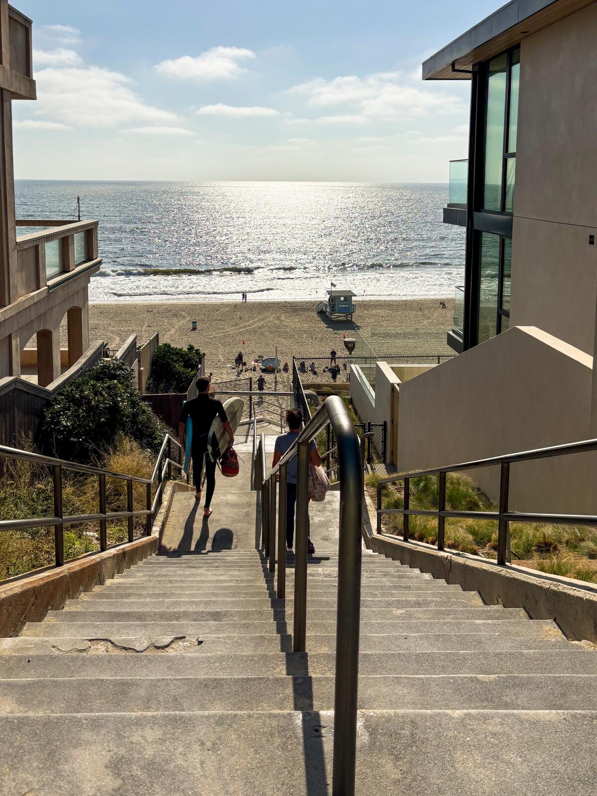 A stairway splits two buildings, leading to the beach and ocean.