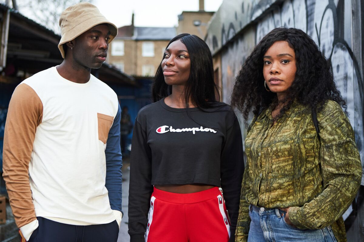 Three friends stand outside by a wall covered in graffiti