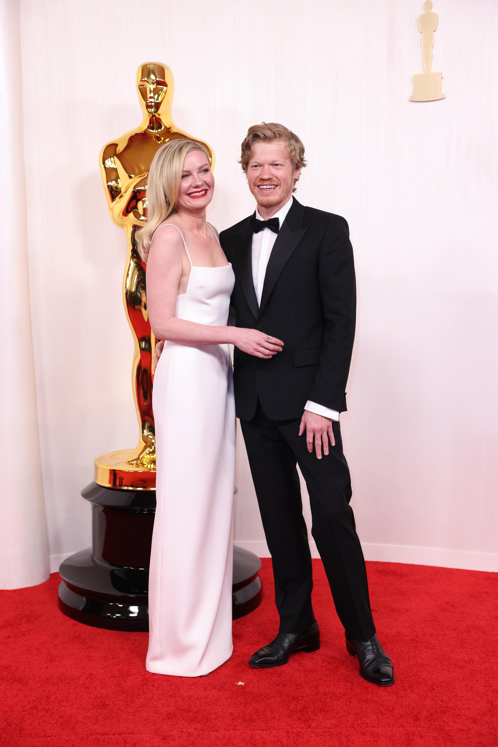 Kirsten Dunst wears a white dress with spaghetti straps, and Jesse Plemons wears a black suit. 
