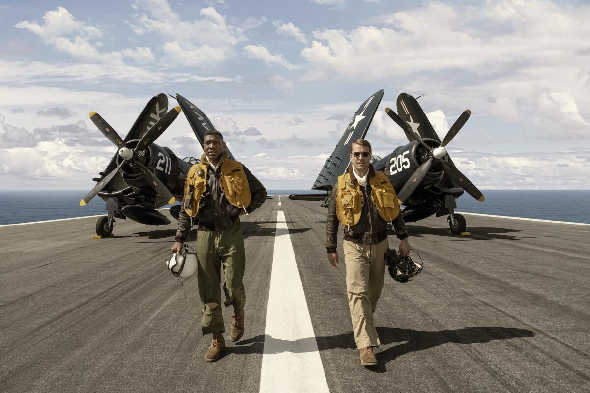 Two Navy pilots walk away from their planes on the deck of an aircraft carrier in the movie "Devotion."