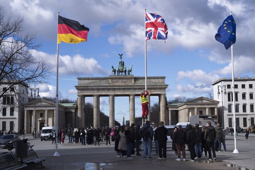 A person raises the Union Jack flag, centre, in front of the Brandenburg Gate at the eve of the visit of King Charles III at the German capital, in Berlin, Tuesday, March 28, 2023. Britain's King Charles III and Camilla, the Queen Consort, will make an official visit to Germany from March 29 to 31, 2023. (AP Photo/Markus Schreiber)
