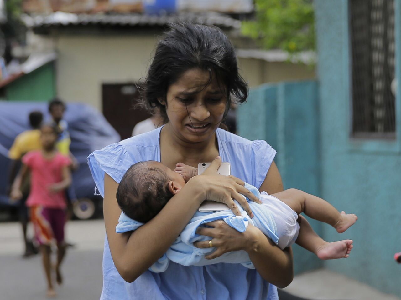 A Sri Lankan woman living near St. Anthony's Shrine hurries away with her infant after police find a device in a parked van in Colombo on April 22. The device was exploded, and there were no casualties.