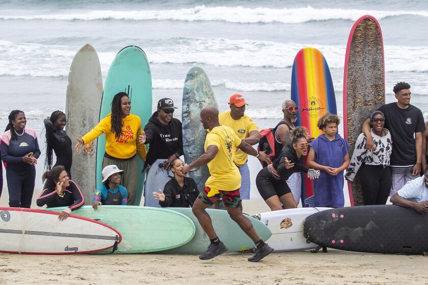 Huntington Beach, CA - Nathan Fluellen, center, founder of "A Great Day in the Stoke," an effort to highlight Black surfers and Black surfing history, high-fives surfers posing for an large group photos during the event at the Huntington Beach pier Friday, June 3, 2022. The event was billed as the "largest gathering of Black surfers in history" and was intended to inspire the Black community to feel welcome in the water and to experience and share the joy of surfing the waves safely as well as paying homage to veteran Black surfers who have been surfing since the 1950's. Surfers started the morning with a surf competition, free yoga lessons, and free surf lessons. The inaugural AGDITS aimed to create a safe space for Black surfers to connect, compete in a surf competition, recognize and award leaders in the community, provide free surf lessons, and capture an iconic photo of 500 black surfers similar to A Great Day in Harlem (1958) and A Great Day in Hip-Hop (1998) A Great Day in the Stoke welcomes all BIPOC (Black, Indigenous, and People of Color) communities and allies to surf in unity. (Allen J. Schaben / Los Angeles Times)