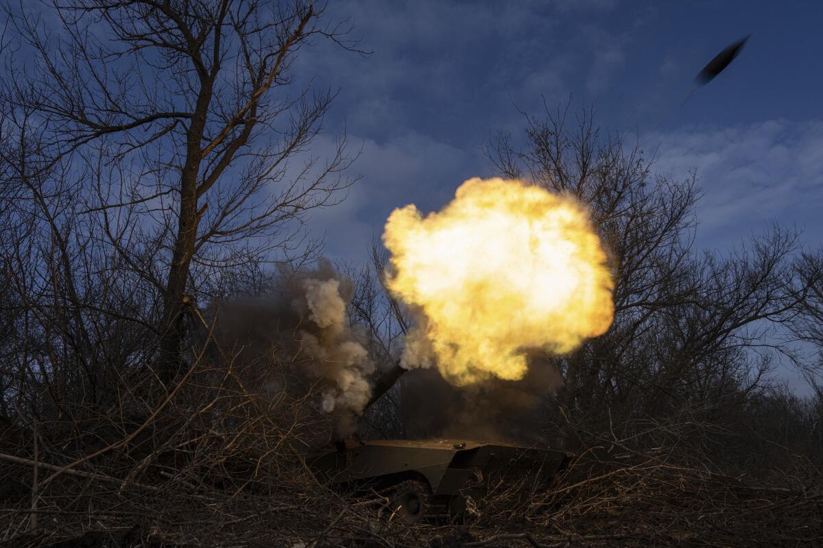 Ukrainians fire a self-propelled howitzer among trees.