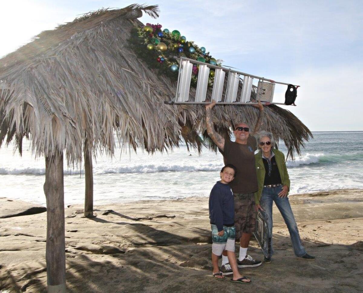 Wreath Returns Cortez Jernigan, his dad Nathan Jernigan and Melinda Merryweather celebrate their Dec. 5 installation of a wreath on the Windansea Shack, which will remain there through New Year’s Day. For 25 years, Merryweather said, she has placed the wreath here, ‘and for many years, no one knew who did it; it just appeared.’ The wreath was donated by Friends of Windansea.