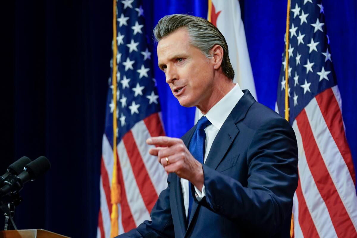 Gov. Gavin Newsom, standing in front of a U.S. flag, gestures while talking.
