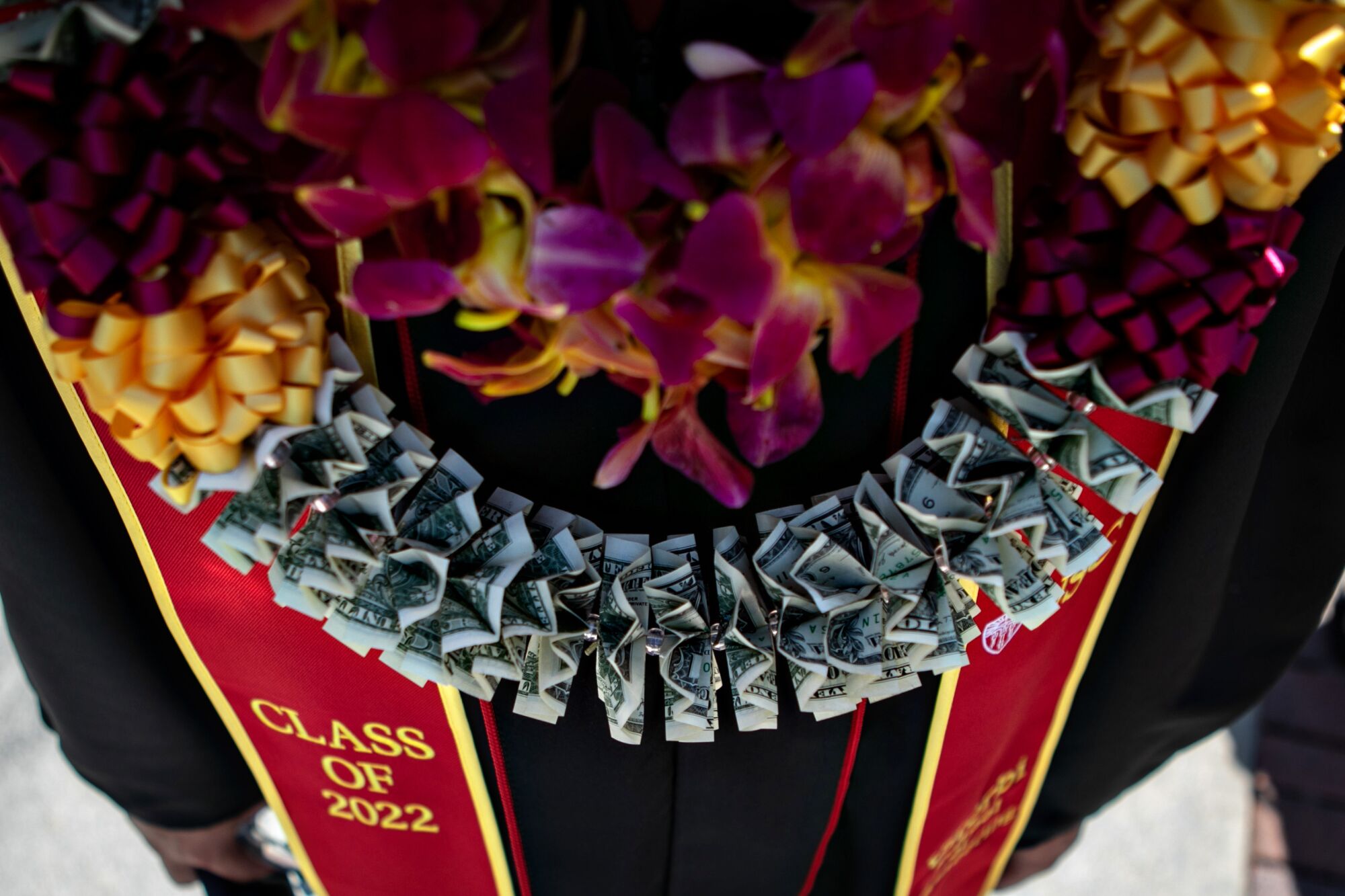 A graduate wears a lei made of flowers and another made of dollar bills