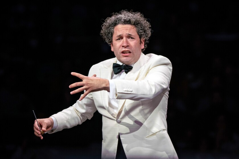 Un hombre con un traje blanco y una pajarita negra dirige una orquesta de una manera animada y emotiva.