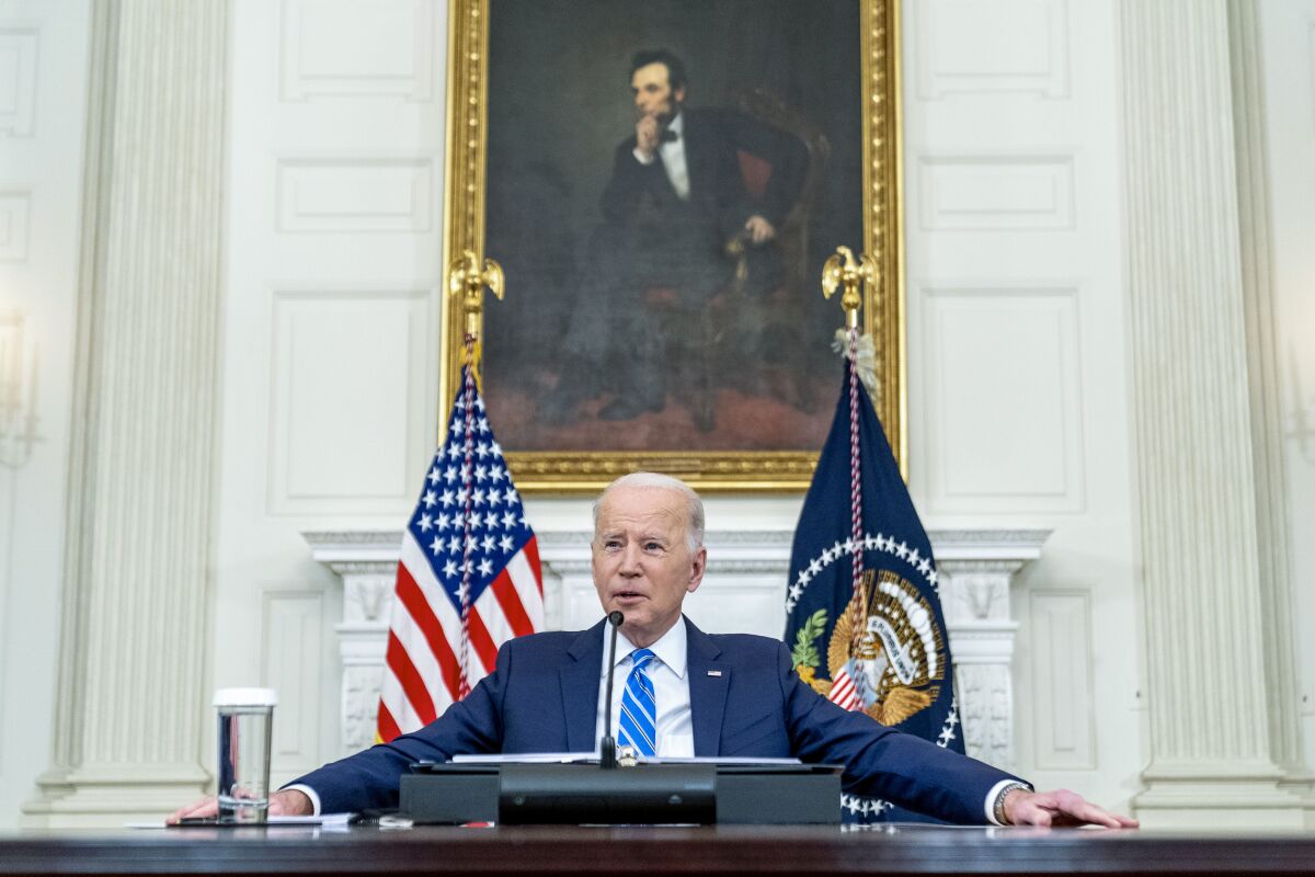 President Biden speaks while seated at a table during a meeting in the State Dining Room.