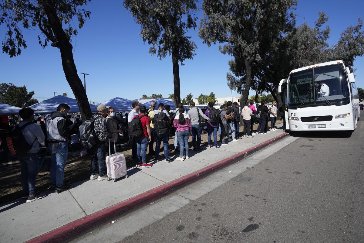 Migrantes hacen fila para tomar un autobús al aeropuerto en San Diego. 