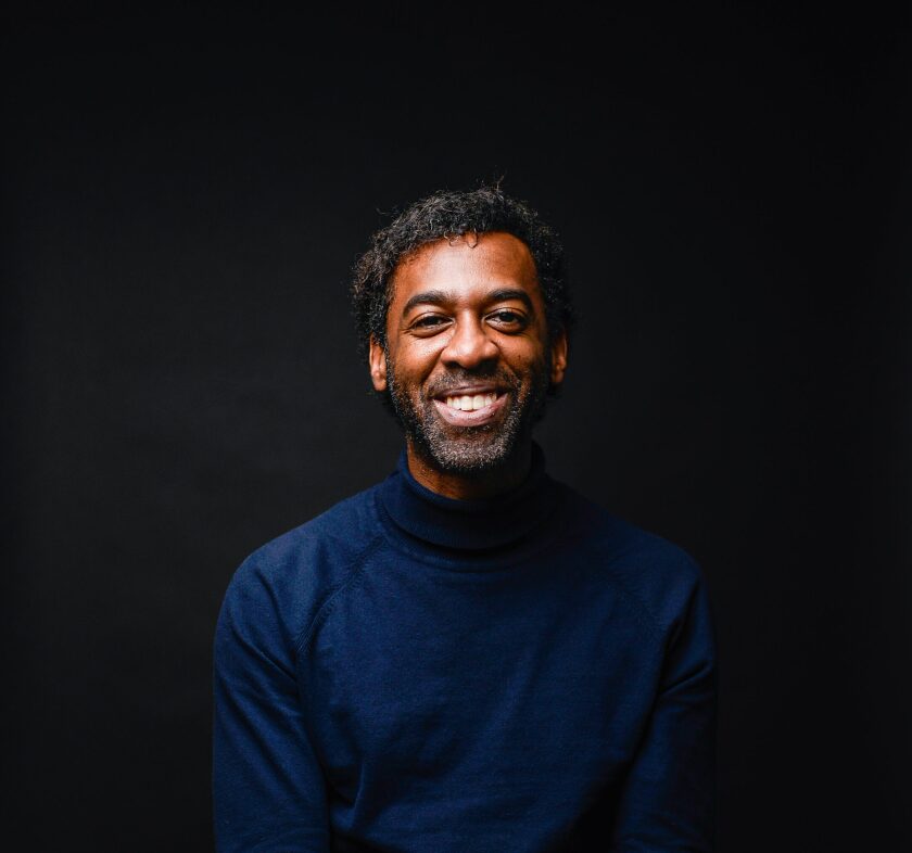 A man in a navy turtleneck in front of a black background