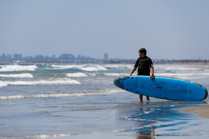 San Diego, CA - June 29: Max Romanillo, 9, of San Diego, holds his board before going into the water as part of YMCA Camp Surf at Imperial Beach on Thursday, June 29, 2023 in San Diego, CA. This was only the third time since December that campers were allowed to swim due to the sewage crisis. (Meg McLaughlin / The San Diego Union-Tribune)