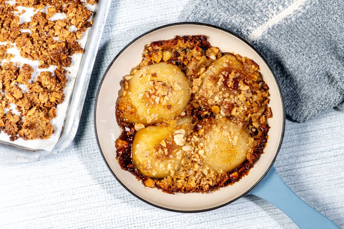 Caramel pear crisp in a bowl, with a tray of extra granola-like topping next to it.