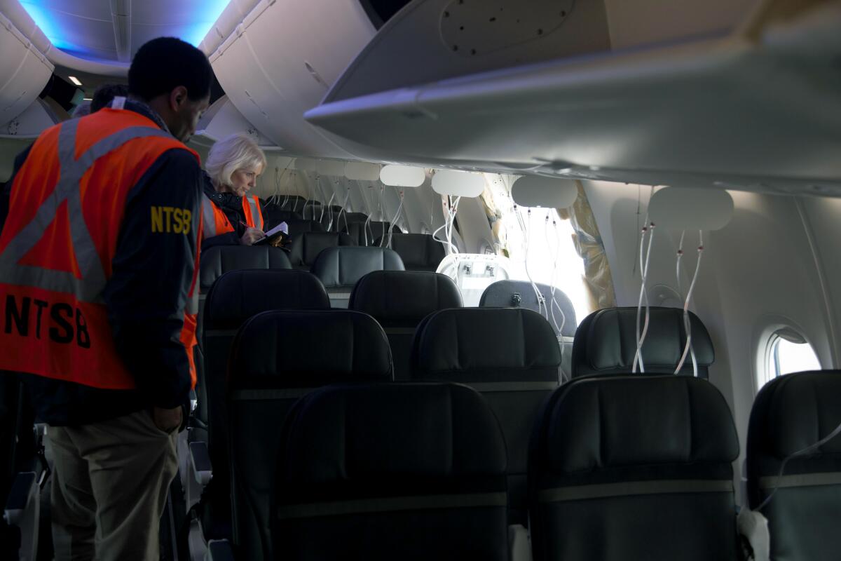 Two people in orange vests stand inside an airline cabin near a gaping hole.