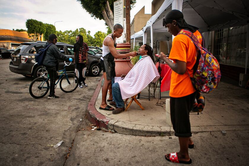 LEIMERT PARK, CA - JUNE 15: Jacket Rashad, a street barber, gives Karim Mejia Mawema, a food vendor, a haircut 
