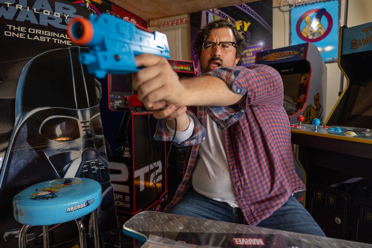 A person in a recording studio holds a blue plastic gun as if shooting it