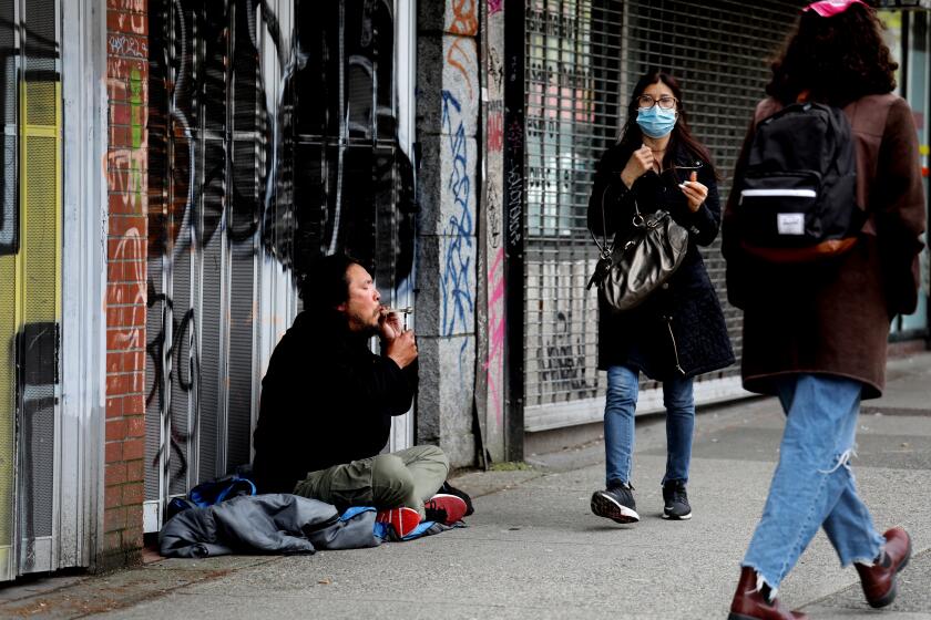 VANCOUVER, BRITISH COLUMBIA - MAY 04: A man, left, smokes drugs through a glass pipe near historic Chinatown in the Downtown Eastside (DTES) neighborhood on Wednesday, May 4, 2022 in Vancouver, British Columbia. Supervised consumption sites in the DTES give addicts who use fentanyl, opioids, crystal methamphetamine and other drugs a place to use and get harm reduction supplies; clean syringes, alcohol swabs, sterile water, tourniquets, spoons and filters. On April 14, 2016, provincial health officer Dr. Perry Kendall declared a public health emergency under the Public Health Act due to the significant rise in opioid-related overdose deaths reported in B.C. since the beginning of 2016. (Gary Coronado / Los Angeles Times)