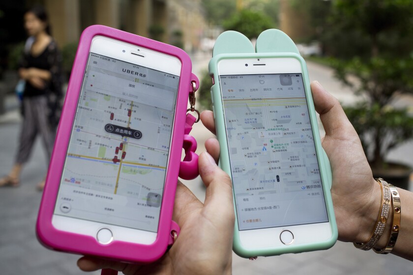 Two smartphones show the ride-hailing apps Uber and Didi Chuxing side by side Monday in Beijing.