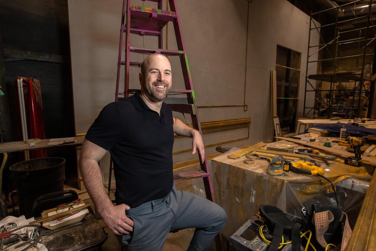 A man leans against a ladder amid the backstage carpentry underway at Pasadena Playhouse.